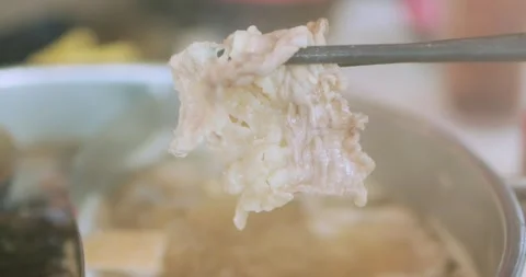 Cooked sliced beef held with chopsticks over a steaming hot pot with broth .. Stock Footage 346686744