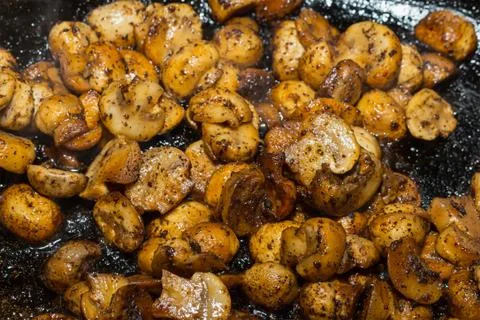 Cooked small fried champignons halves in spices and oil on a dark background Stock Photos