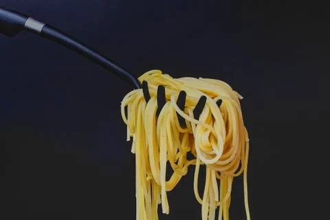 Cooked spaghetti on spaghetti spoon. Spaghetti on black background. Dark food Fotos de archivo