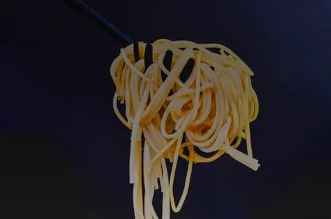 Cooked spaghetti on spaghetti spoon. Spaghetti on black background. Dark food Stock-Fotos