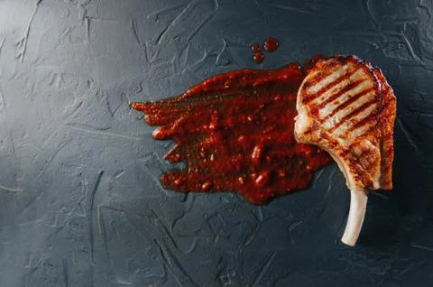 Cooked steak on the bone on a dark blue background with a red sauce of tomatoes 写真素材