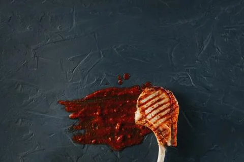 Cooked steak on the bone on a dark blue background with a red sauce of tomatoes 库存照片