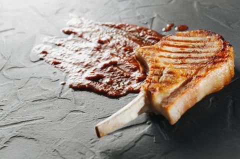 Cooked steak on the bone macro shooting with red tomato sauce. Conceptual photo Stock Photos