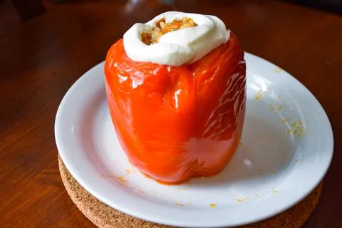 Cooked stuffed red pepper topped with a dollop of sour cream on a white plate Stock Photos