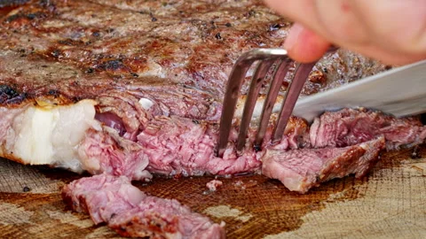 Cooked veal steak on the grill is cut into pieces with a knife. Stock Footage 249886545