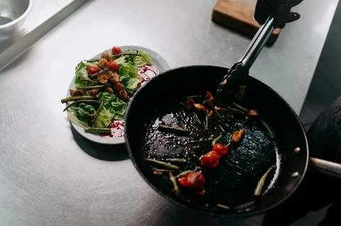 The cooked vegetables in the pan are placed on a plate. Salad preparation pro Stock Photos