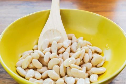 Cooked white beans are placed in a yellow bowl along with a wooden spoon. Veg Stock Photos
