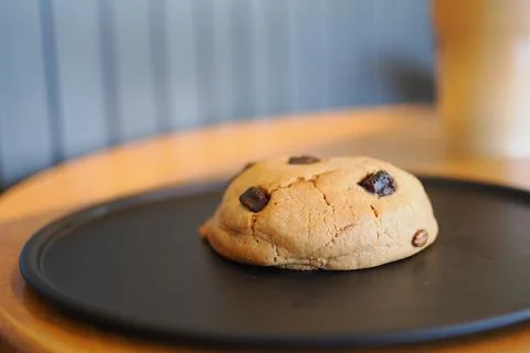 Cookie on a black plate in a cafe setting with a drink in the background Stock Photos
