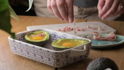 Cooking Avocado with Egg and Bacon. The girl prepares a healthy meal, close-up Stock Footage 272634397