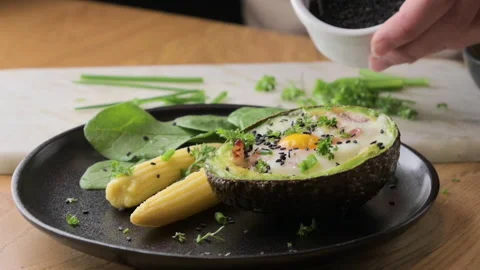 Cooking Avocado with Egg and Bacon. The girl prepares a healthy meal, close-up Stock Footage 272764203