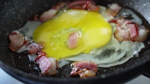 Cooking bacon and eggs in a frying pan Video stock 299433175