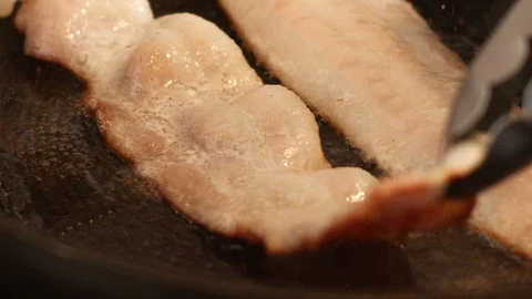 Cooking bacon in slow motion watching grease pop Stock Footage 117902933