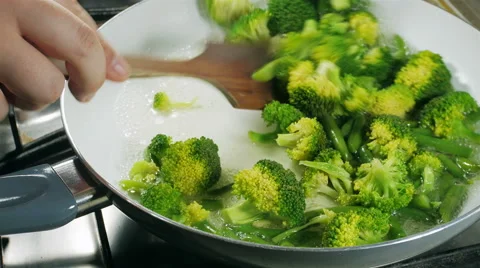 Cooking broccoli and green beans in a frying pan. Stirring with a wooden spoon. Stock Footage 57532922
