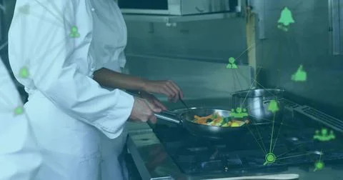 Cooking chefs wearing chef jackets stirring veggies in frying pan at gas range Stock Photos