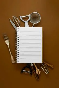 Cooking concept. Kitchen tools and empty note book. Brown background. Stock Photos