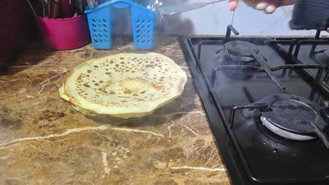 Cooking crepes in the kitchen using a frying pan on a gas stove during day time Stock Footage 328444601