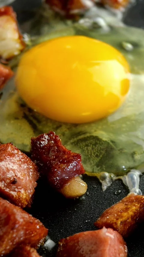 Cooking delicious hot dishes. Fried eggs or omelette and diced, crispy, sausage Stock Footage