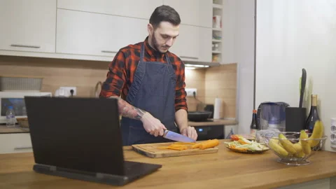 Cooking dinner in modern kitchen reading recipe from a laptop Video stock 143789317