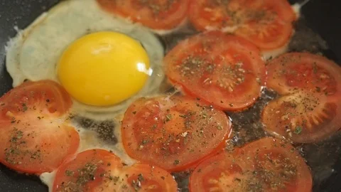 Cooking fried eggs with tomatoes and basil. Girl breaks two eggs Stock Footage 104976426