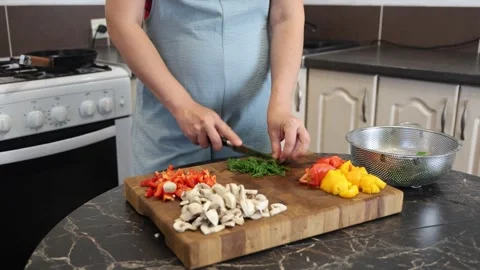Cooking fried eggs with vegetables at home. A woman chops vegetables on a wooden Stock Footage 317543493
