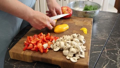 Cooking fried eggs with vegetables at home. A woman chops vegetables on a wooden Stock Footage 317544072