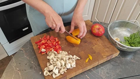 Cooking fried eggs with vegetables at home. A woman chops vegetables on a wooden Stock Footage 317544884