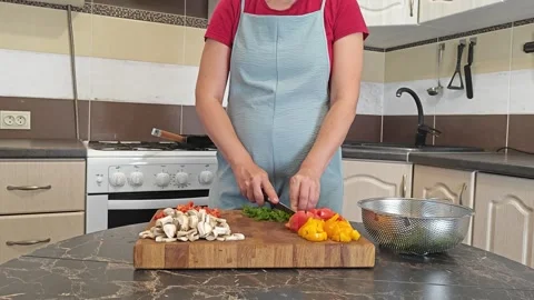 Cooking fried eggs with vegetables at home. A woman chops vegetables on a wooden Stock Footage 317544888