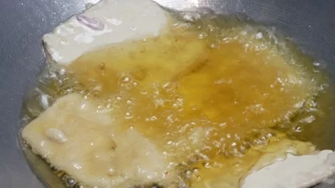 Cooking fried tempeh coated with wheat flour in hot oil in a frying pan Stock Footage 302944034