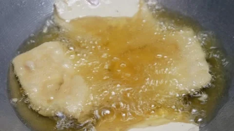 Cooking fried tempeh coated with wheat flour in hot oil in a frying pan Stock Footage 302944172