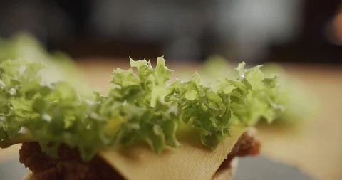 Cooking hamburger. Close-up of chef hands puts half bun on cutlet, cheese and Stock Footage 116178496