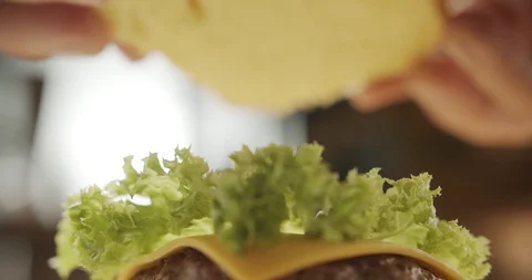 Cooking hamburger. Macro shot Chef hands closes juicy burger with half bun. 4K Stock Footage 116178176