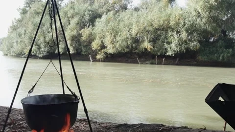 Cooking on a hanging cauldron over a fire, on the banks of a beautiful river Vídeos de archivo 257046305