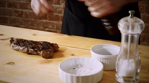 Cooking meat. Cook adding black pepper to a juicy grilled beef steak. 4K Vídeo Stock 84265864