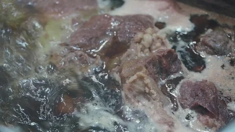 Cooking meat in a pot with water and steam rising in a kitchen setting Stock Footage 346580964