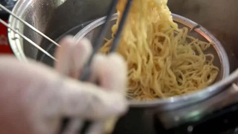 Cooking noodles while stirring using chopsticks and placing them in a bowl Stock Footage 272297917