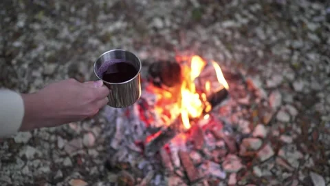 Cooking on an open fire in the forest. The person holds a metal mug over the Stock Footage 164902120
