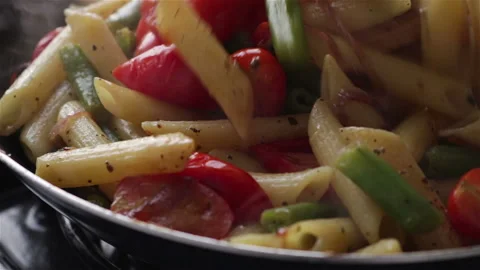 Cooking penne pasta with vegetables frying pan extreme close up Stock Footage