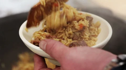Cooking of pilaff with lamb. Man putting cooked pilaff with mutton in a plate 库存影片 63662216