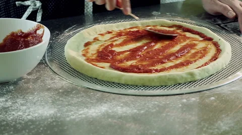 Cooking pizza. Female hands adding and spreading tomato sauce on tasty pizza. HD Stock Footage 68991546