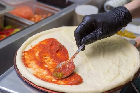 Cooking pizza, spreads the first layer of tomato. Stock Photos