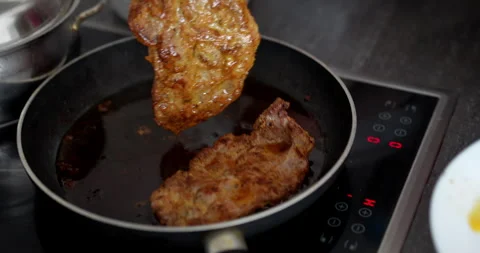 Cooking pork chops in a pan on induction stove in a Kitchen during the Day Stock Footage 321096690