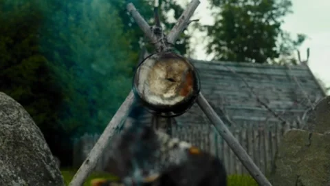 Cooking pot hanging over campfire in historical setting Stock Footage 313323828