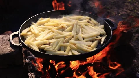 Cooking potatoes in a cast iron pan over an open campfire Stock Footage 338998312