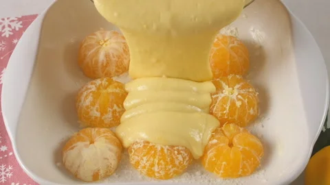 Cooking pouring cake batter over peeled mandarin oranges in baking dish. Stock Footage 317235192