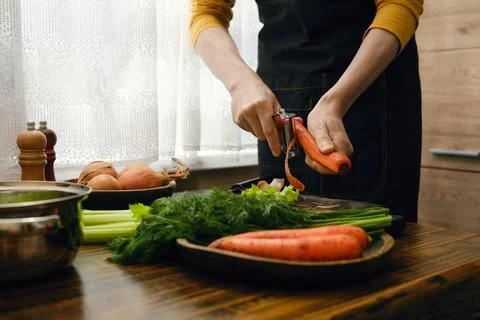 Cooking preparation involves peeling carrots and chopping vegetables in a k.. Фото