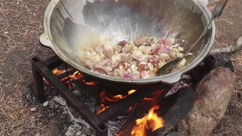 Cooking process frying beef  and onion in large cauldron on open fire outdoor Stock Footage 119432196