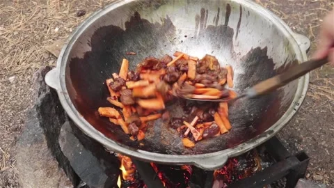 Cooking process frying beef  and carrot in large cauldron on open fire outdoor Stock Footage 124269073