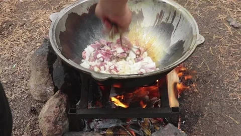 Cooking process frying beef meat and onion in large cauldron on open fire Stock Footage 116776608