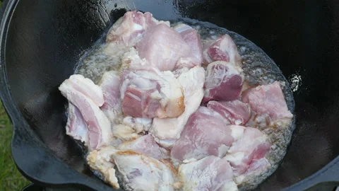 Cooking process, frying pork meat in large cauldron on open fire Stockbeeldmateriaal 131540725
