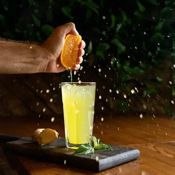 Cooking process of ginger lemonade. Man squeezing orange juice into glass with a Stock Photos